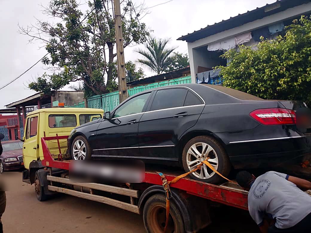 Sanglage d'une Mercedes Classe E noire sur plateau avant le départ, Yaoundé
